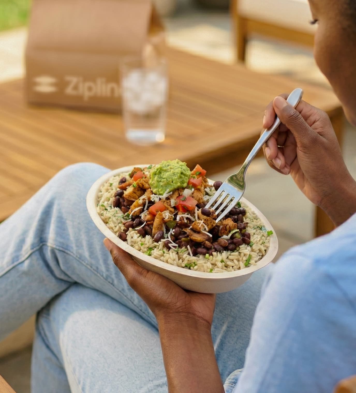 Person eating a burrito bowl outdoors with a Zipline delivery bag in the background.