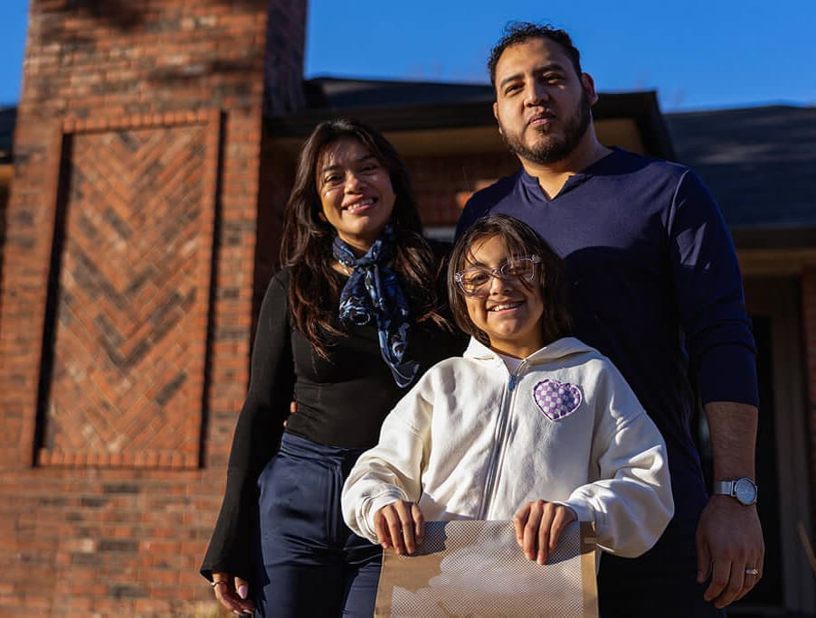Family smiling outside their home in Dallas holding a delivery bag.