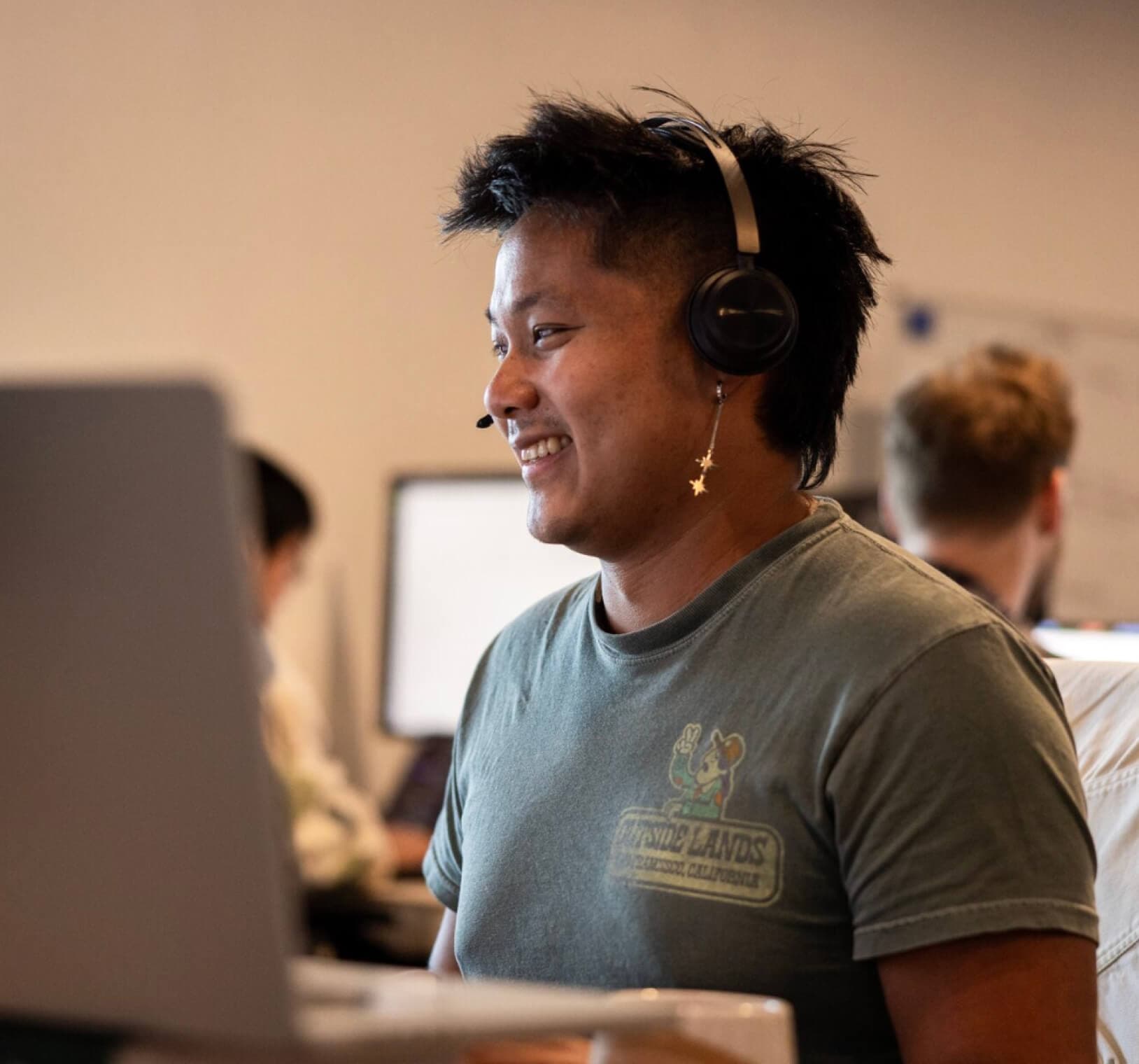 Person smiling at a desk wearing headphones in an office.