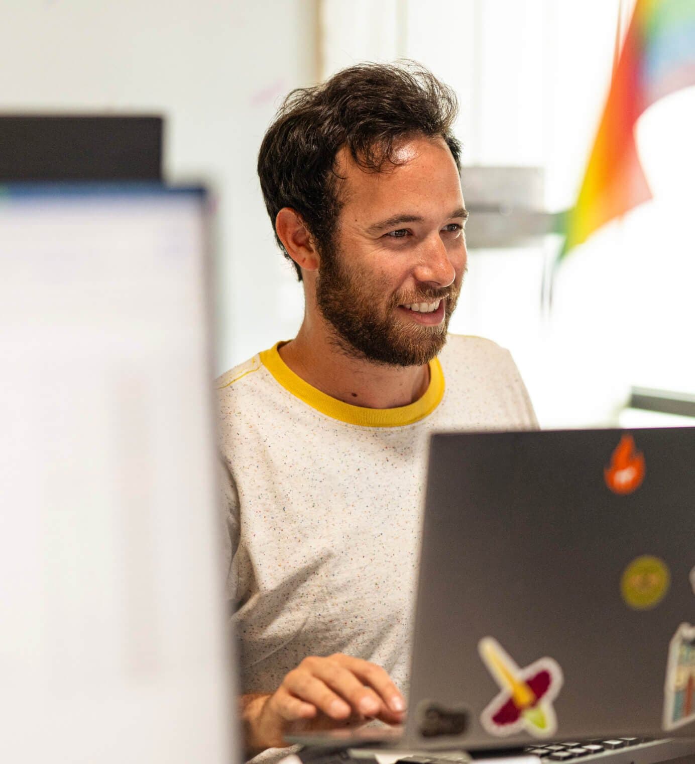 Man smiling while working on a laptop with stickers at an office desk.