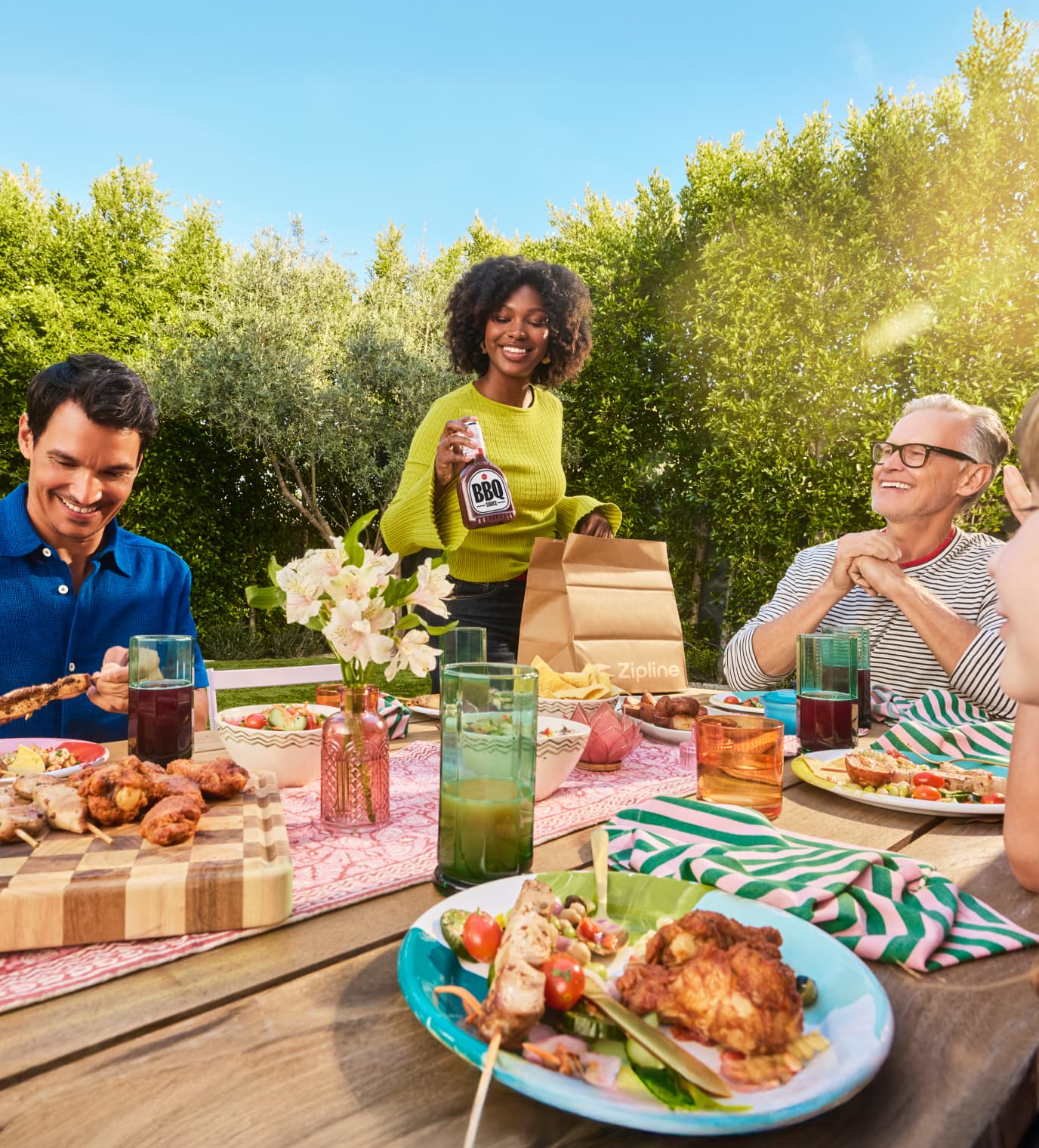 Group enjoying an outdoor meal as someone pulls BBQ sauce from a Zipline delivery bag.