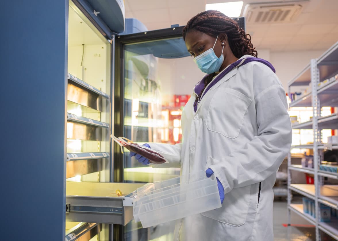 Healthcare worker in mask and gloves handling a blood bag in a medical storage facility.