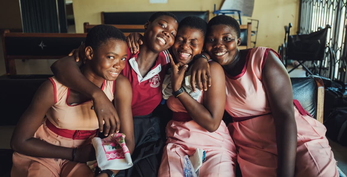 Group of four people smiling and embracing indoors.