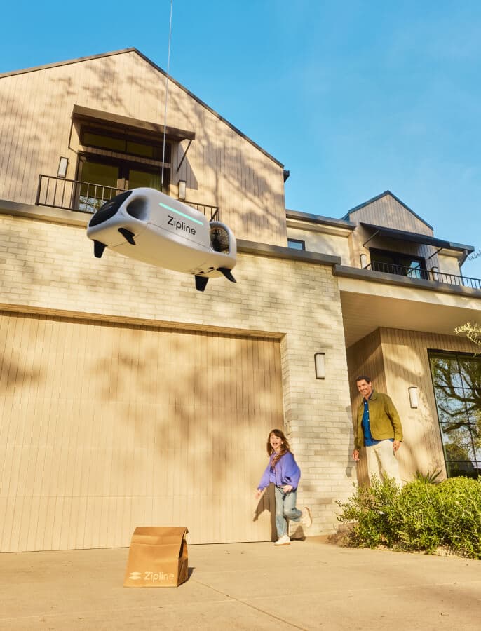 Zipline drone hovering above a delivered package outside a residential backyard.