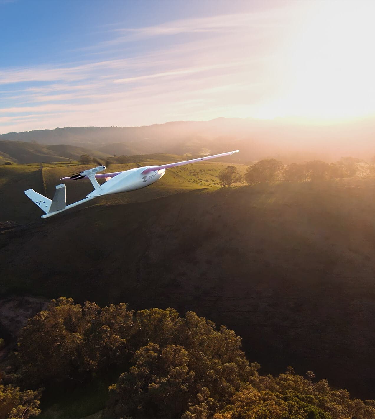 Zipline delivery drone flying over green rolling hills at sunset.
