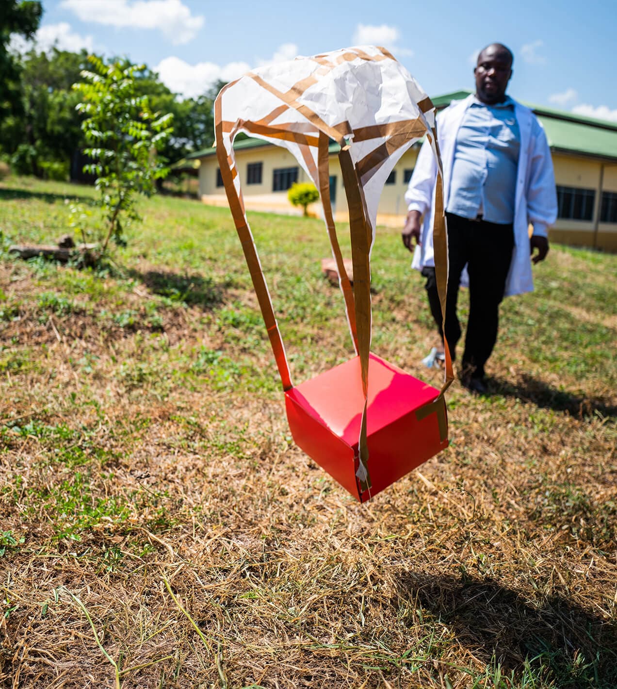 A red delivery package landing via parachute as a healthcare worker approaches.