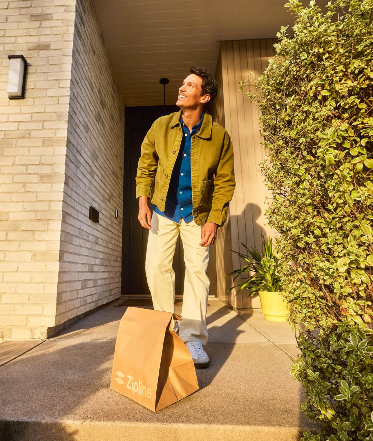 Person looking up and smiling next to a Zipline delivery bag at their front door.