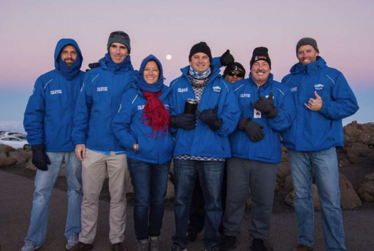 Group of people wearing Skyline blue jackets in front of the sunrise in Haleakala National Park.